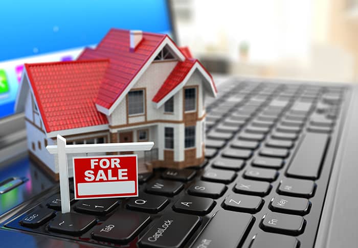 a miniature home with a for sale sign on top of a laptop